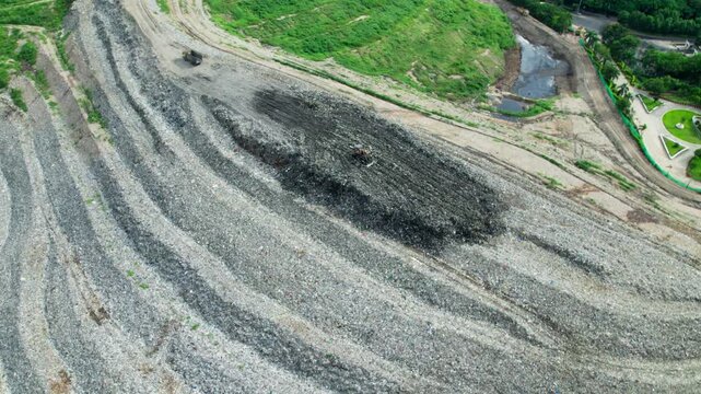 JCB and Tipper working in large scale of Dumping Yard with layered waste deposits and uneven terrain. day time, bird eye view, push in shot, drone shot, 4k.