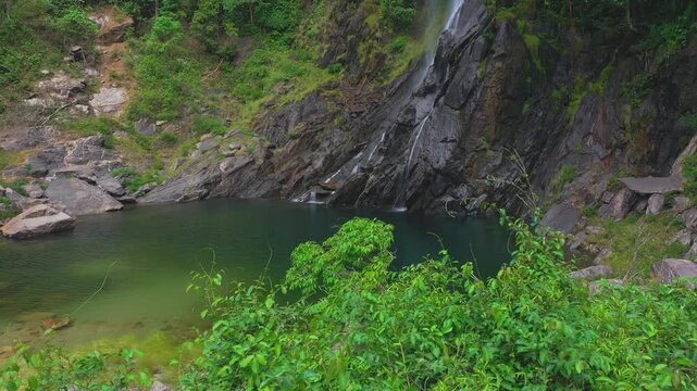 Low pull-away drone shot of pristine emerald pool and jagged quartzite base of the Cato&aacute; Waterfall in Campo Alegre, Tocantins, capturing the raw, secluded beauty of the Serras Gerais region.