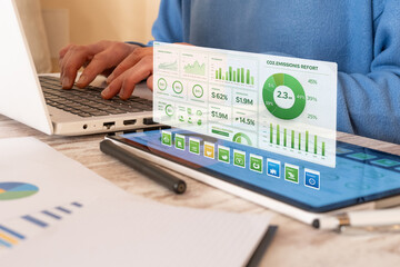 Person typing on a laptop, analyzing an immersive digital esg report with co2 emissions, financial data, and sustainability metrics for corporate responsibility and green business strategy