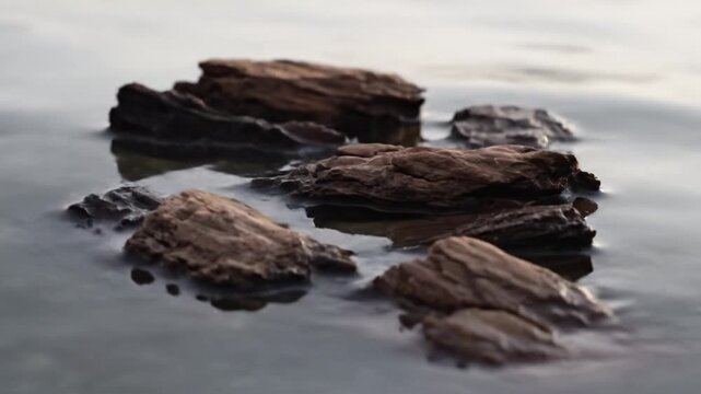 Brown layered sediment rock formation calm water reflection wet stone shoreline textured smooth shallow water weathered erosion muted color peaceful dusk natural layered rock shoreline calm reflection