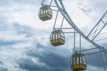 Yellow passenger cabin ferris wheel with dramatic cloudy sky background in amusement park