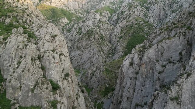 Slow cinematic glide into a rocky chasm in Uzbekistan shows layered limestone, stream beds and grass on ledges. The valley draws toward Chimgan peak while warm morning light opens a panorama