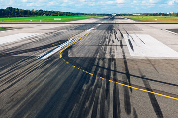 Black skid marks streak across a worn runway, framed by white and yellow aviation lines. Runway...