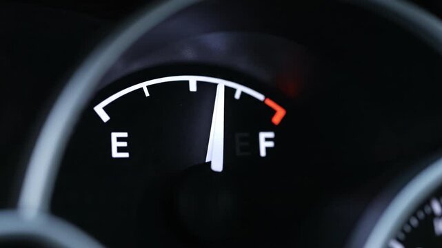 Fuel gauge needle near full illuminated empty and full letters red warning segment plus low fuel dashboard needle near empty dark interior instrument meter gas sense of travel readiness and caution