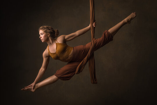 Graceful aerialist performing a split on flowing silks &mdash; dramatic studio portrait showcasing strength, flexibility, balance and movement in earthy tones
