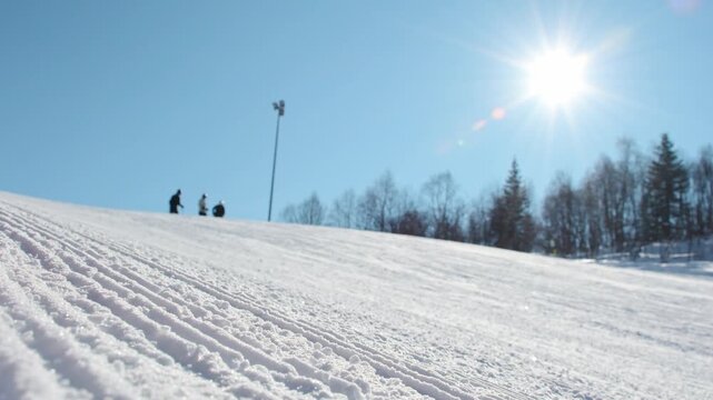 Group of beginners ski downhill on snow slope under bright winter sun with fresh groomed piste surface and clear blue sky, mountain ski scene.Intentional blur out of focus effect unrecognizable skiers