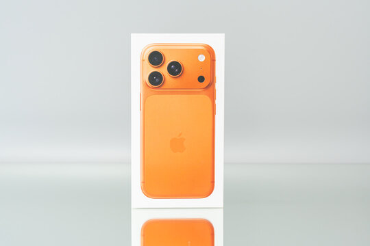 Germany Berlin December 25, 2025. Front view of the Apple iPhone 17 Pro orange box centered in a minimalist studio scene. Bright color contrasts with the neutral reflective background.