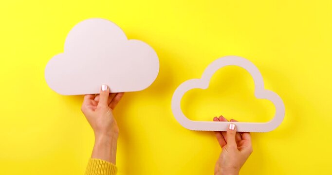 4K footage of two hands holding cloud symbols against a yellow background, representing cloud storage, additional memory, data, or digital storage concepts.
