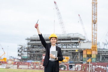 An Asian female engineer coordinates the operation of machinery in an industrial power plant, utilizing radio communications, safety awareness, and technological advancements.