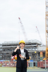 A female engineer manages an industrial plant construction project amidst cranes and heavy machinery, demonstrating professionalism, strategic business planning, and a modern environment.