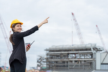 An Asian female engineer works on an industrial construction site, communicating with her team via radio, focusing on machine control processes, industrial safety standards, and engineering leadership