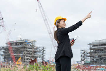 A female engineer wearing a safety helmet is overseeing operations at an industrial plant construction site, demonstrating smart thinking, business efficiency, and innovative development.