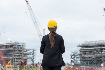 The image shows the back of a female engineer operating heavy machinery in an industrial power plant, managing the operation of modern systems and developing future infrastructure.