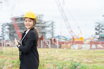 Asian female engineer coordinating industrial construction activities for her company, integrating business objectives, machinery supervision, and professional engineering standards.