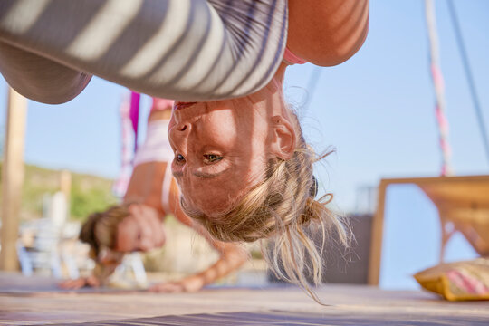 Close up view of a mature woman hanging upside down from a yoga hammock during an outdoor aerial yoga class.