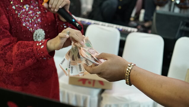 One hand gives money (5000 rupiah Indonesian currency) to the other hand
