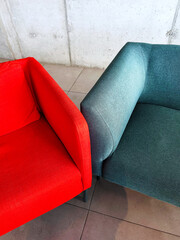 Two modern armchairs in contrasting red and teal colors stand side by side in a minimalist interior