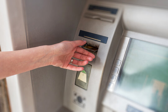 A person's hand inserting a credit card into an automated teller machine to perform a banking transaction.