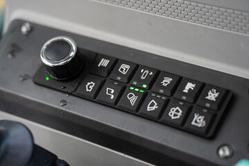 Detailed view of construction excavator control panel featuring joystick buttons, rotary selector, and active status lights inside operator cabin