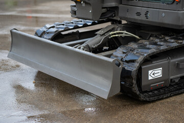 Industrial excavator undercarriage featuring front dozer blade and tracked drive system on paved ground, focused on construction machinery durability