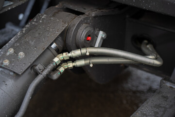 Industrial excavator hydraulic system detail featuring flexible hoses, metal couplings, and wet surface, focused on heavy equipment engineering reliability