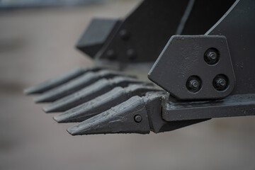 Industrial excavator bucket teeth detail with reinforced steel points and bolts, highlighting heavy construction equipment components for ground excavation