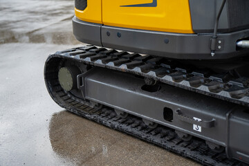 Detailed view of construction excavator rubber track system and undercarriage frame on wet ground, highlighting heavy equipment traction and stability