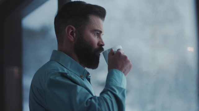 Serene moment of man with coffee in snowy landscape, Calm artist savoring warm drink by window amidst winter outside