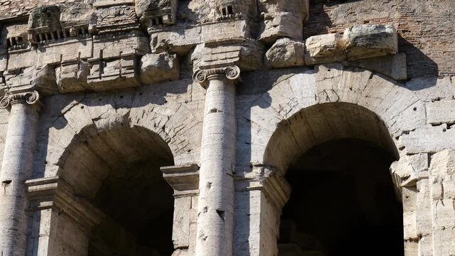 ancient roman fa&ccedil;ade weathered stone arches eroded ionic capitals crumbling decorative blocks below brick walls modern tall windows up close rome empire 