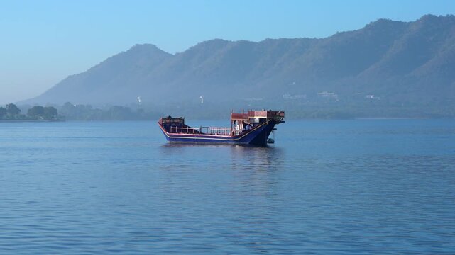 Traditional boat floating on Lake Pichola with mountain backdrop, Udaipur, Rajasthan, India