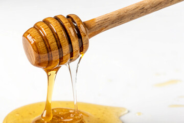 Golden honey slowly dripping from a wooden honey dipper against a white background.