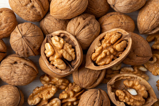 Pile of whole and halved walnuts on white background.