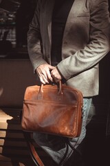 Elegant man in a stylish coat and suit holding a premium leather briefcase. Conceptual photography of business travel, fashion, and professional lifestyle.