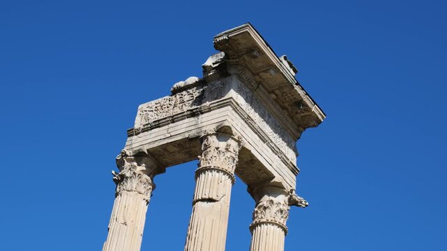 three weathered corinthian columns topped by ornately carved entablature floral reliefs contrasts sharply brilliant cloudless blue sky rome up close empire 