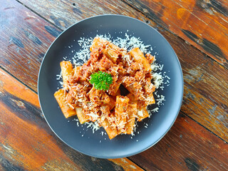 Top view of pasta with tomato sauce, parmesan cheese, and minced pork served with rigatoni on a wooden table, classic Italian food.
