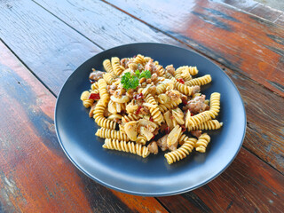 A side view of pasta featuring fusilli tossed with chili, garlic, olive oil, and Italian sausage, offering a mildly spicy flavor, served on a wooden table. Classic Italian cuisine.