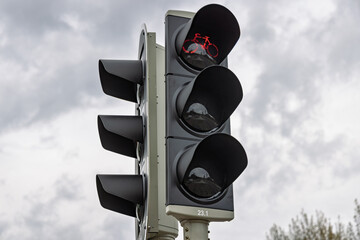 A close-up of a Dutch traffic light for cyclists showing a red LED bicycle icon against a cloudy sky, indicating cyclists must stop and wait.