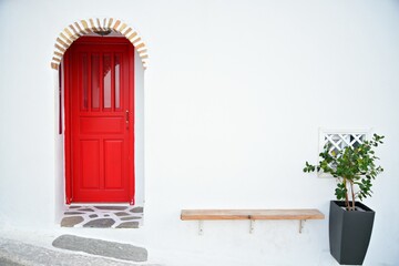 Picturesque arched red wooden door with a stone trim on a whitewashed wall in Chora the capital of...