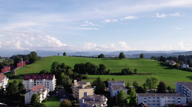 Flying towards a green hill with a small white house and alps in the background, Switzerland