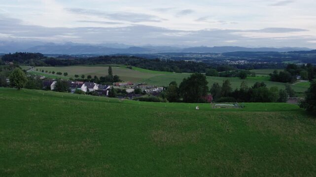 An artist is walking on top of a green hill while holding a canvas, Switzerland