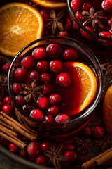 Mulled wine. The rich, red liquid with slices or whole oranges and cranberries floating within it. The background is filled with spiced sticks like star anise 