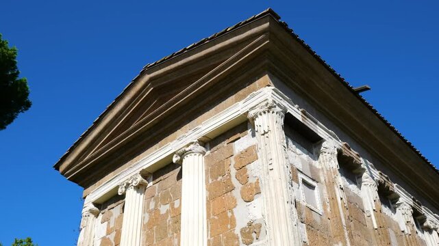 classical temple fa&ccedil;ade triangular pediment weathered stone walls complemented by tall fluted corinthian columns ornate capitals under bright blue sky rome italy roman ancient 