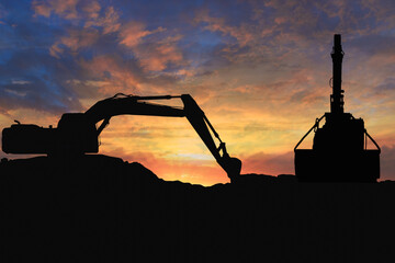 Crawler excavators silhouette are digging the soil in the construction site. With blue sky and clouds of on sunset background