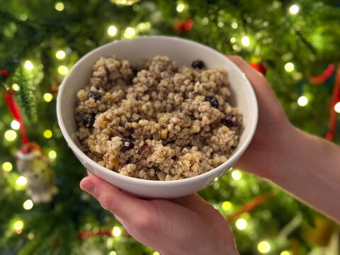 Traditional Ukrainian Christmas dish Kutya made of boiled wheat, poppy seeds, candied fruits and walnuts in white plate on Christmas tree background 