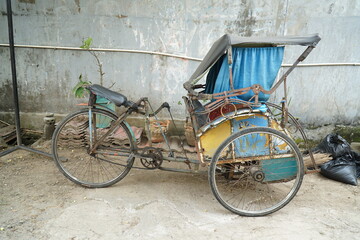 a rickshaw, a traditional Indonesian three-wheeled means of transportation, parked next to the house
