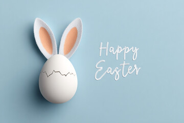a cracked white egg with fluffy bunny ears attached sits on a blue background with the words Happy Easter written in white script