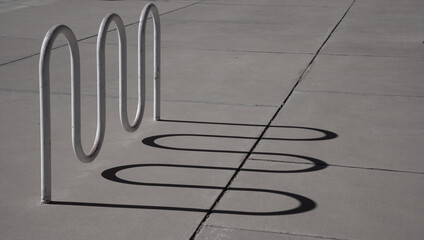 curved or wavy shadow lines on the pavement of a bicycle rack or curved installation on the sidewalk outdoors curved shadow lines horizontal backdrop background or wallpaper