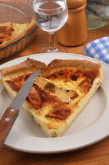 Part de tarte au camembert dans une assiette avec un couteau servie &agrave; table avec un verre d'eau en gros plan