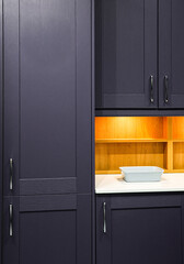 Contemporary home kitchen interior featuring dark purple wood cabinets, white countertop and warm...