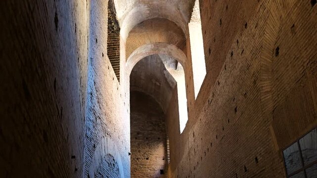narrow ancient brick corridor high arched ceilings illuminated by sunlight streaming through irregular windows weathered hole pocked walls rome italy hole-pocked surfaces 